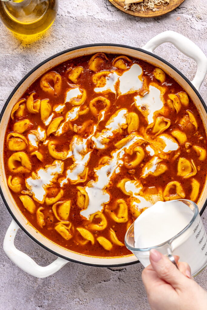 cream being added into a tomato-based tortellini soup.