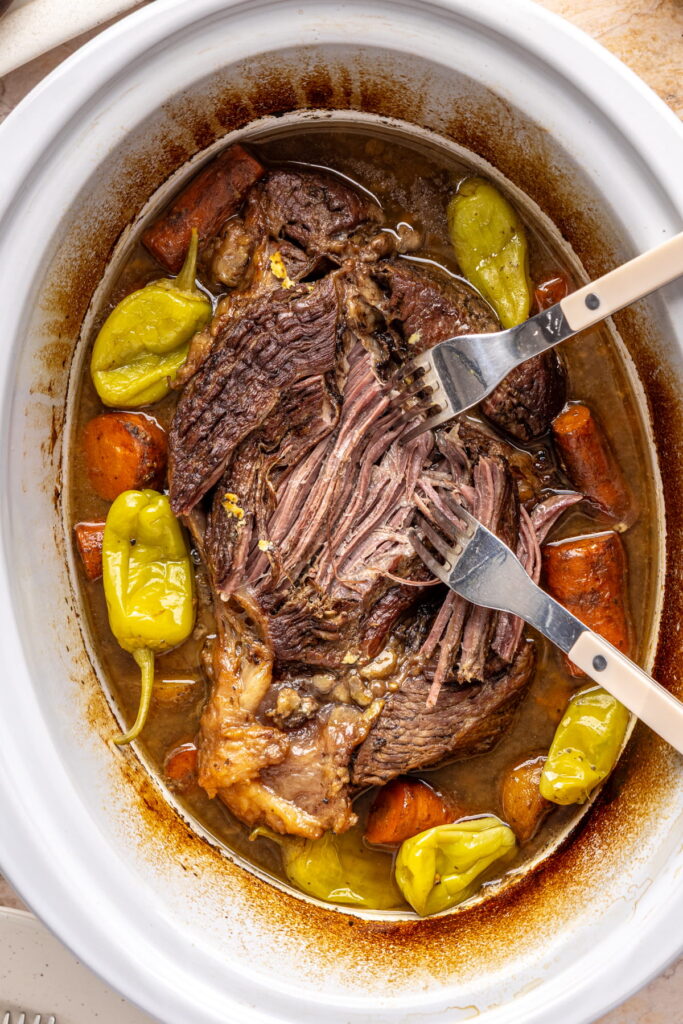 Mississippi pot roast being shredded with two forks in a slow cooker