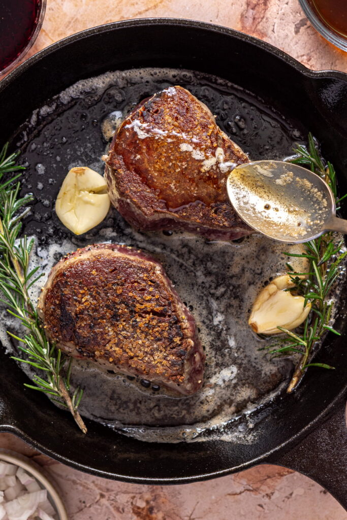 filet mignon being basted in a pan with butter, herbs, and garlic