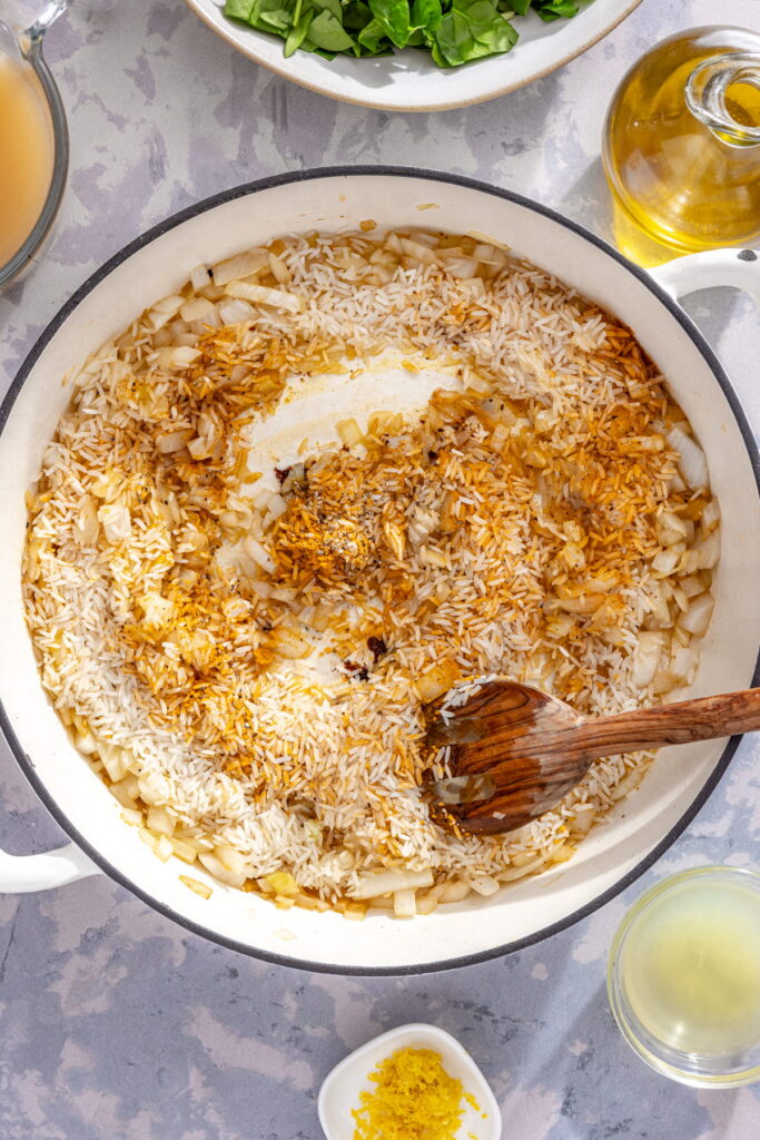 turmeric, rice, onion, and garlic being stirred in a pan