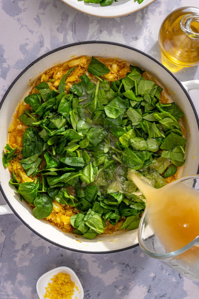 spinach and broth being added to a pan with rice
